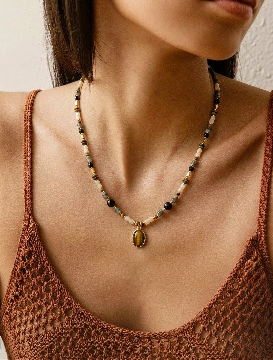Femme portant le collier ras de cou BOIS DE NUIT, bijou bohème chic avec pendentif Œil de tigre et agate noire.